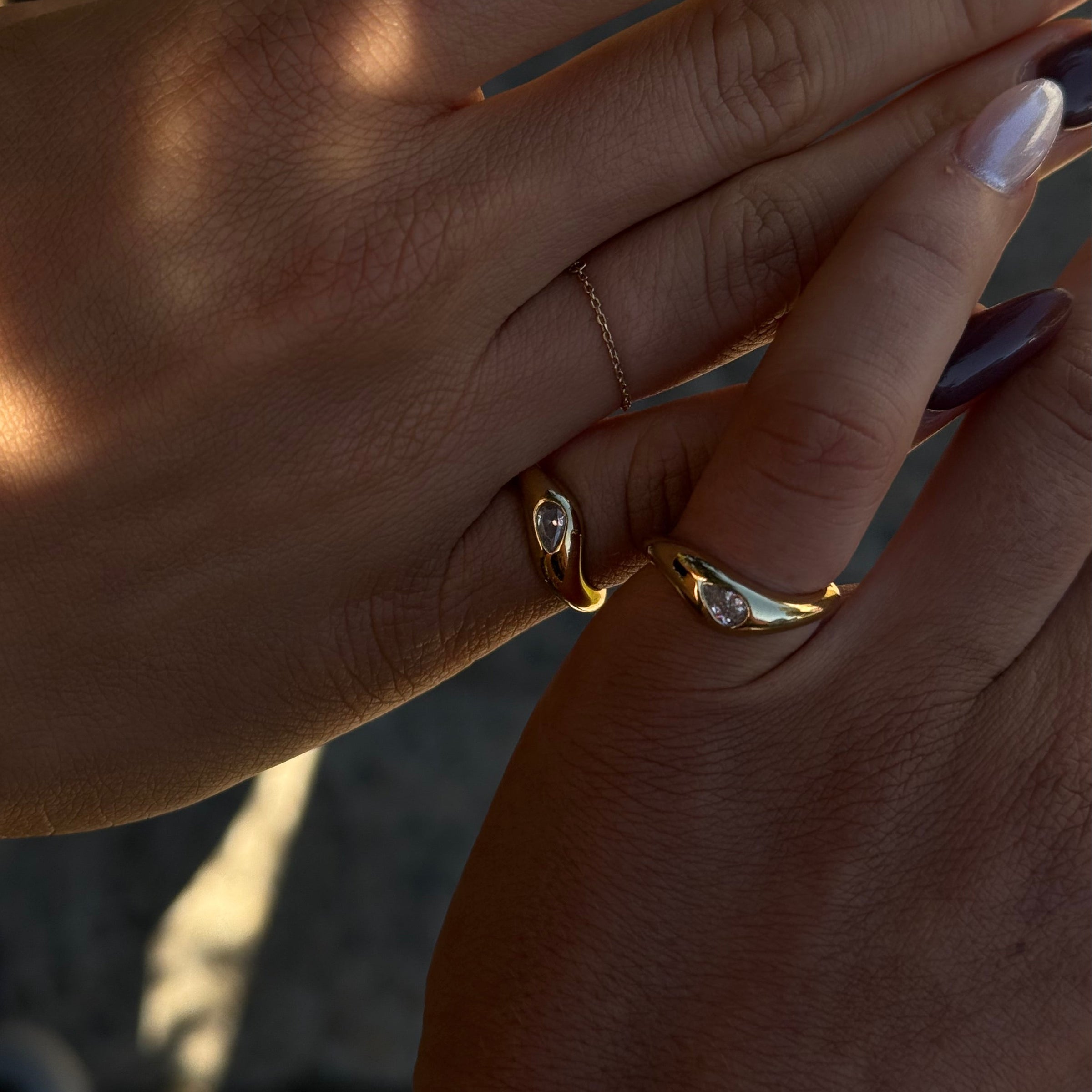 Close-up of hands wearing gold rings with clear stones in natural sunlight. Matching friendship rings